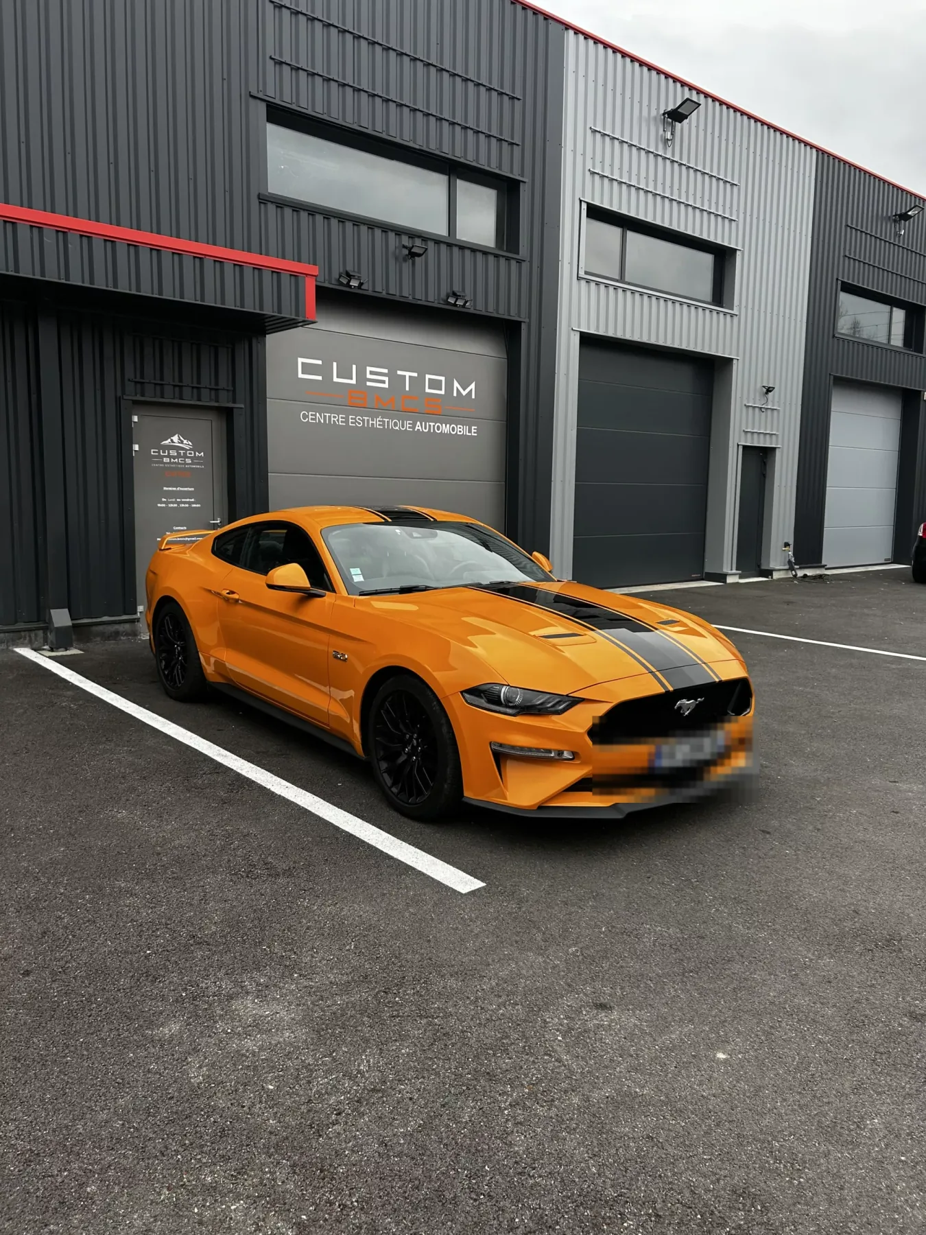 Devanture de l'atelier Custom BMCS avec une Ford Mustang GT orange